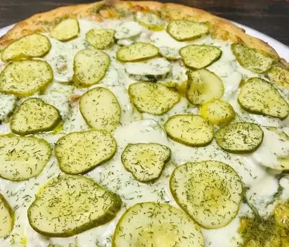 A pizza with pickles and cheese on a plate.